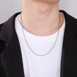 Close-up of a silver stainless steel wheat chain necklace worn over a white t-shirt