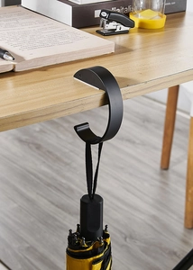 Close-up of a black portable desk hook holding a bag on a wooden table edge