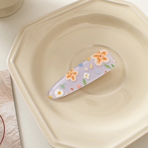 Close-up of a purple acrylic hair clip with cartoon flower patterns on a beige tray