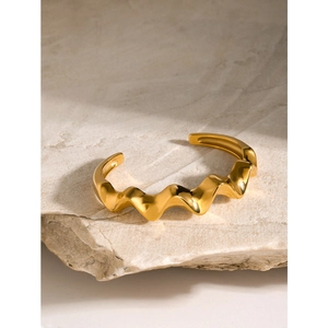 Polished 18k gold stainless steel wavy bangle on stone base with natural lighting