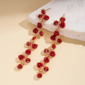 Gros plan de boucles d'oreilles dorées à roses rouges et gemmes sur marbre