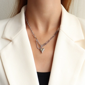 Silver necklace detail with asymmetric chain and heart pendant worn on white blazer