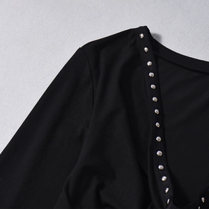Macro detail of silver rivets on black long-sleeved top with premium knit texture