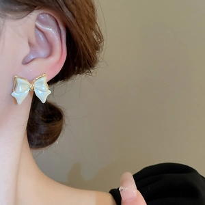 Minimalist cream bow earrings with gold plating shown on model in a soft profile view