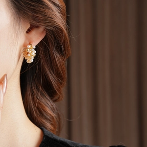 Detail view of U-shaped gold earrings with pearls and zircons worn by a model