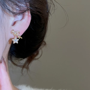 Close-up of a gold bow and star earring with cubic zirconia on a female model