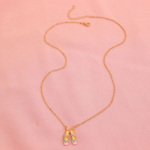 Detail of golden ballet slippers pendant with pink accents and crystal studs on a fine chain