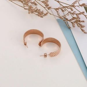 Close-up of rose gold C-shaped hoop earrings with intricate woven texture and hollow design