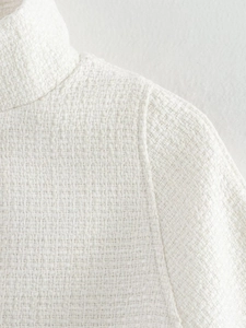 Close-up of white tweed fabric texture and woven neckline detail on a women's cape coat
