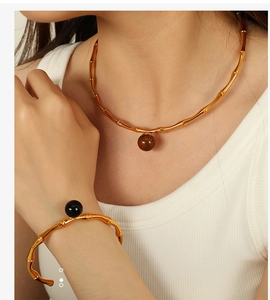 Detail of golden bamboo style neck collar and cuff bracelet with dark spherical charms