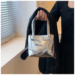 Detail of silver metallic handbag featuring bow decoration and chain shoulder strap
