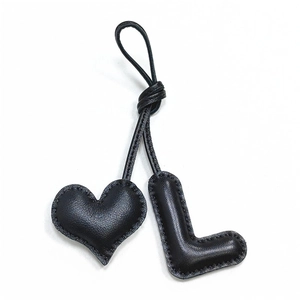 Detail of handmade black leather bag charm featuring a heart and letter L with fine stitching