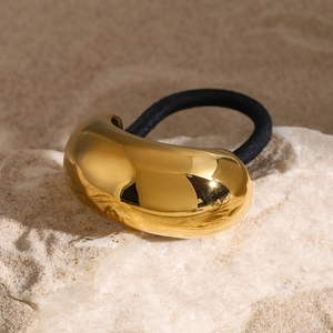 Minimalist golden bean-shaped stainless steel hair tie on a white stone background