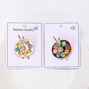 Detail of two palette-shaped enamel brooches with cat eye stones on a display card