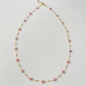 Detail of a golden necklace featuring pink and purple beaded flower charms on flat background