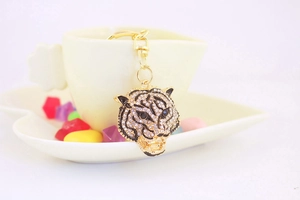 Macro detail of diamond-encrusted tiger head keychain with gold chain on white cup