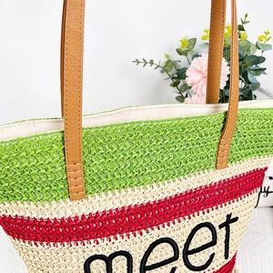 Detailed close-up of woven tote bag with green stripes, leather handles and embroidered text