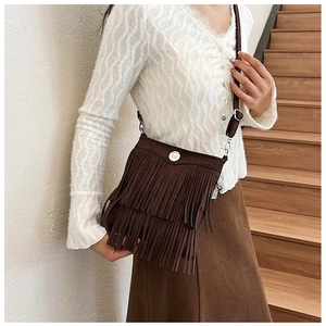Detail of brown suede crossbody bag featuring retro tassel design and adjustable strap