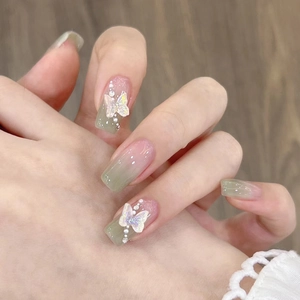 Detail view of green gradient press-on nails with 3D butterfly charms and pearl accents