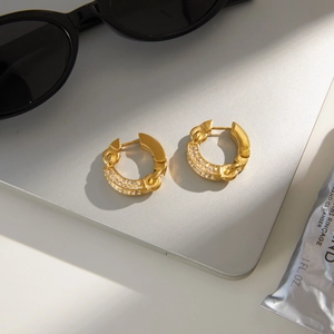 Close-up of golden chunky chain hoop earrings with white zircon pavé on a laptop surface