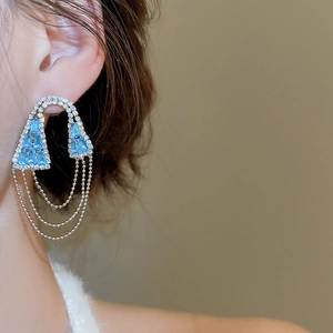 Détail rapproché de boucles d'oreilles à pompons argentés avec zircons géométriques bleus