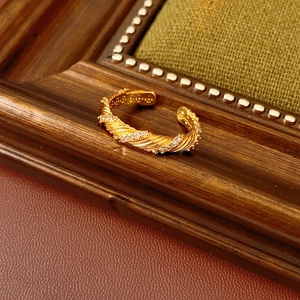 Close-up of golden twisted open ring with inlaid zircons on a vintage fabric background