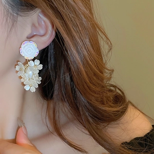 Detail view of elegant white acrylic flower tassel earrings worn by a female model