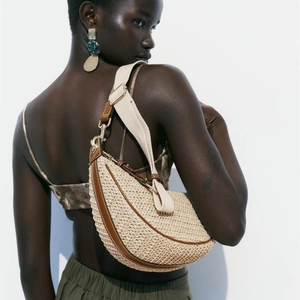 Beige half-moon straw woven shoulder bag with brown leather trim and wide fabric strap