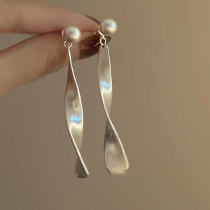 Macro shot of silver pearl drop earrings with elegant wavy metal ribbon pendants