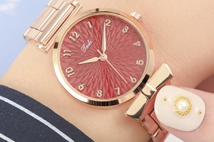 Detailed macro view of rose gold watch with red dial and delicate bow-shaped strap detail