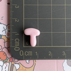 Detailed macro view of a small pink resin T-shaped letter accessory on a centimeter scale mat