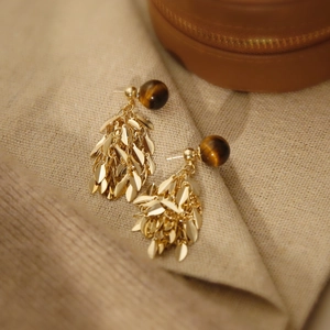 Macro shot of tiger eye resin bead earrings with golden leaf tassels on a leather box
