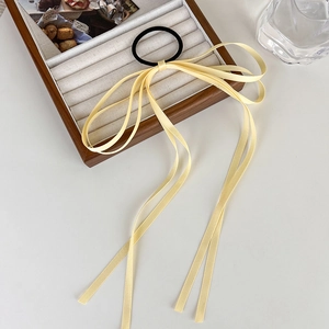 Close-up of long pale yellow silk ribbon bow hair tie on a wooden jewelry display tray