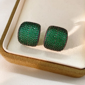 Détail macro de boucles d'oreilles carrées vintage avec zircons verts sur or noir