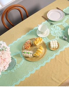 Close-up of mint green lace table runner with floral hollow patterns on a yellow tablecloth