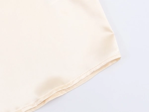 Detaillierte Nahaufnahme der Saumnaht an einem glatten, cremefarbenen Satinhemd für Damen