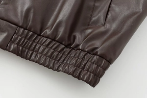 Macro detail of elastic hem on dark brown faux leather bomber jacket with fine stitching