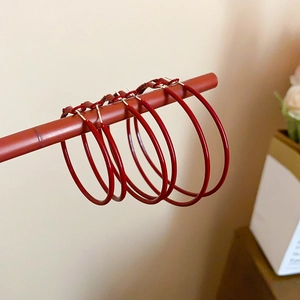 Detailed close-up of three sizes of minimalist red hoop earrings on a brown display rod