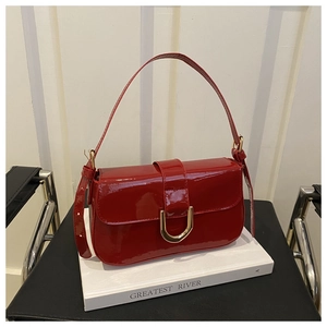 Close-up of red patent leather handbag with gold horseshoe buckle on white books