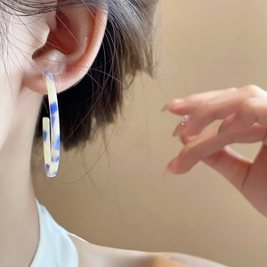 Close-up of blue and white marble resin C-shaped hoop earrings on a model's ear