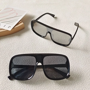 Detailed view of two oversized black flat top driving sunglasses with polished frames