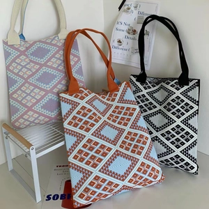 Close-up of geometric knit tote bags in pink, blue, and black displayed on a white shelf
