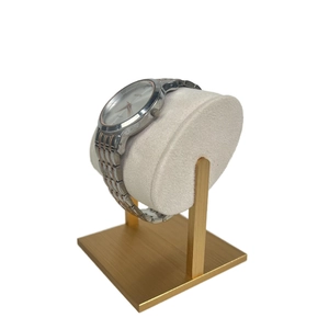 Detail of metal watch stand featuring a white velvet pillow and gold base for jewelry