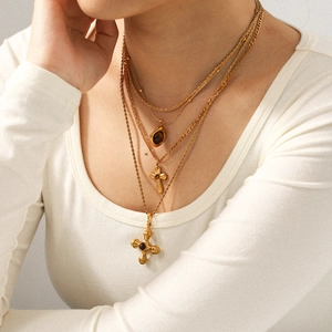 Detailed view of triple-layered gold titanium necklace with tiger eye and cross pendants