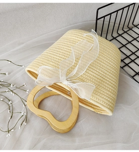 Detail of beige woven handbag with heart-shaped wooden handle and white ribbon bow decoration