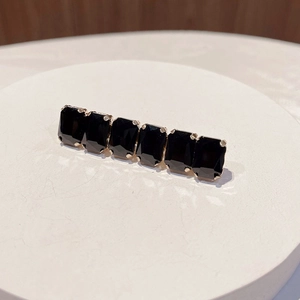Close-up of gold hair clip with black rectangular rhinestones on a white ceramic tray