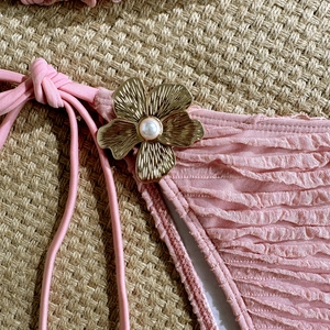 Detail of pink ruched bikini bottom with gold flower ornament and pearl accent