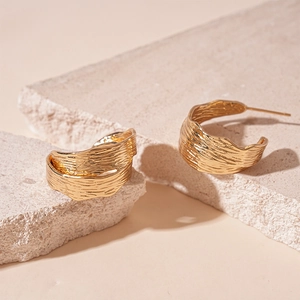 Detailed view of golden C-shaped metal earrings with irregular pleated texture on stone