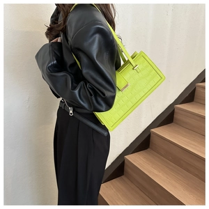Detail of neon green underarm bag with crocodile texture and metallic accents