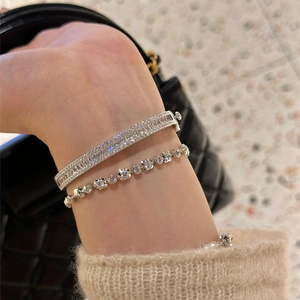 Détail d'un jonc en argent serti de zircons et d'un bracelet tennis portés en superposition